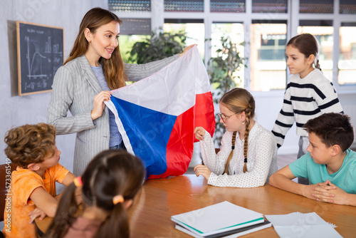Group of preteen schoolchildren attentively watching pedagogue describing Czech flag in schoolroom