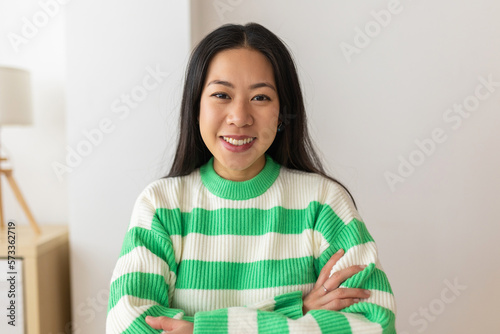 Headshot cute portrait of smiling young adult chinese woman smiling at camera sitting on table at home. Asian people concept