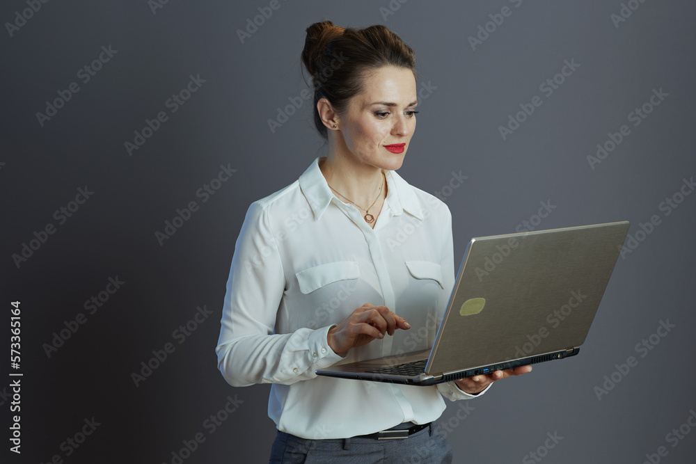 40 years old woman employee using laptop isolated on grey 40 years old woman employee using laptop isolated on grey
