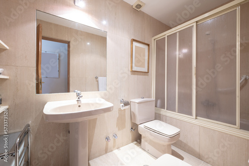 Bathroom with matching pedestal porcelain sink  walk-in shower with tub  large frameless mirror  and light tile