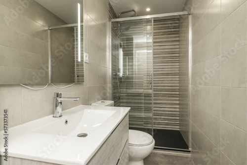 Small bathroom with one-piece resin sink on a cabinet with drawers  glass-enclosed shower stall  and trellis tiles