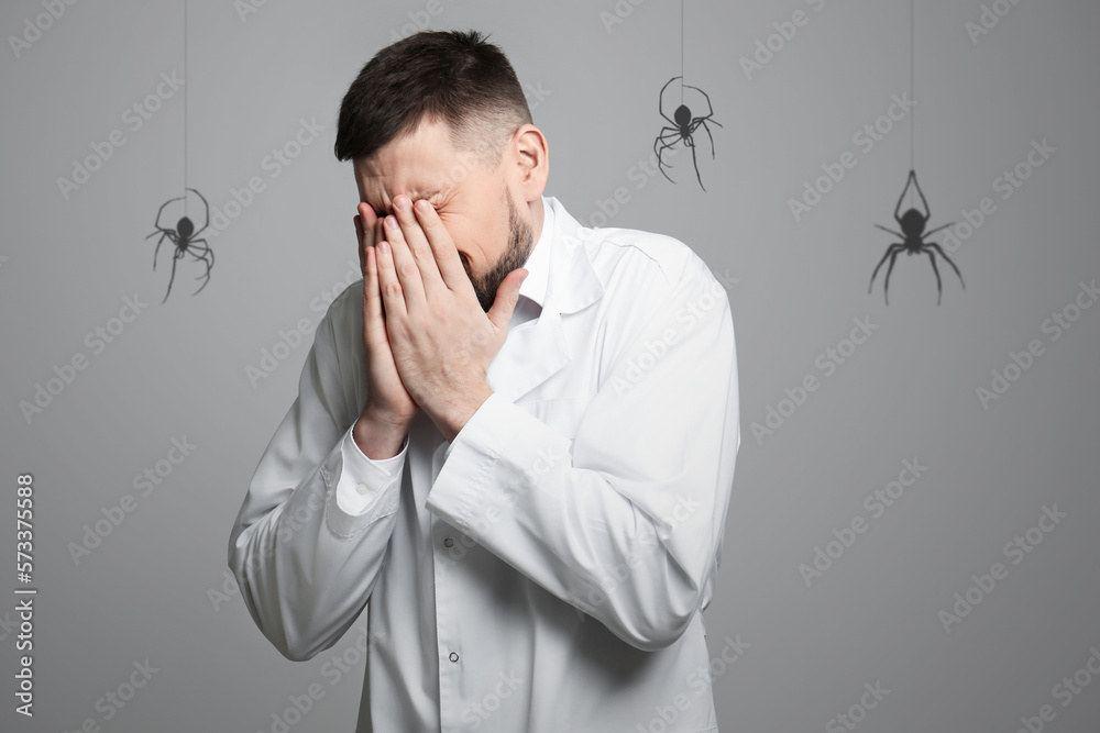 Obraz premium Scared man suffering from panic attack on grey background. Shadows of spiders symbolizing fear and anxiety