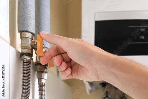 Man turning on valve of gas boiler indoors, closeup