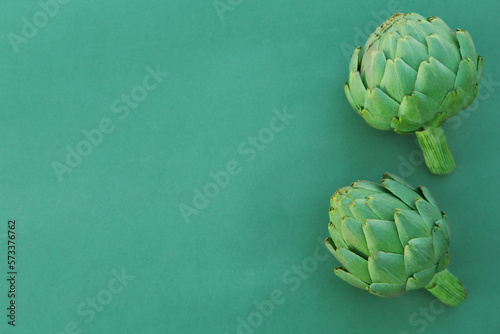 Whole fresh raw artichokes on green background, flat lay. Space for text