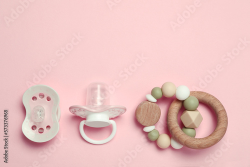 Flat lay composition with pacifiers and other baby stuff on pink background. Space for text