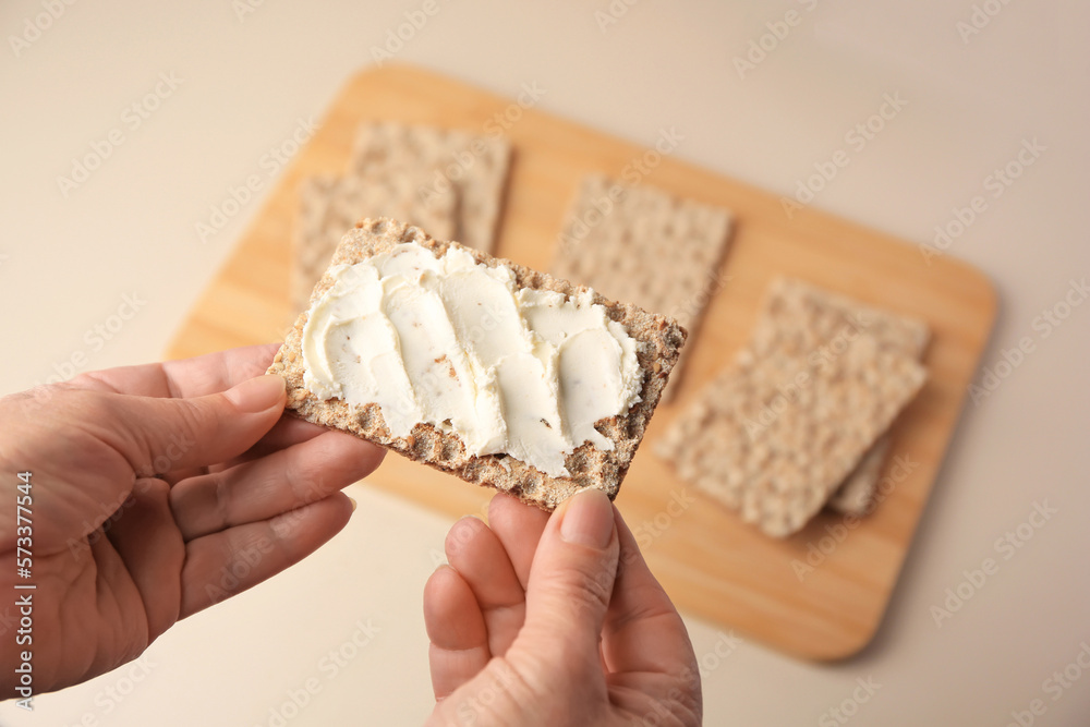 Woman holding fresh crunchy crispbread with cream cheese above table, closeup. Space for text