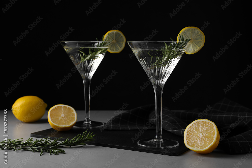 Martini glasses of refreshing cocktail decorated with lemon slices and rosemary on grey textured table