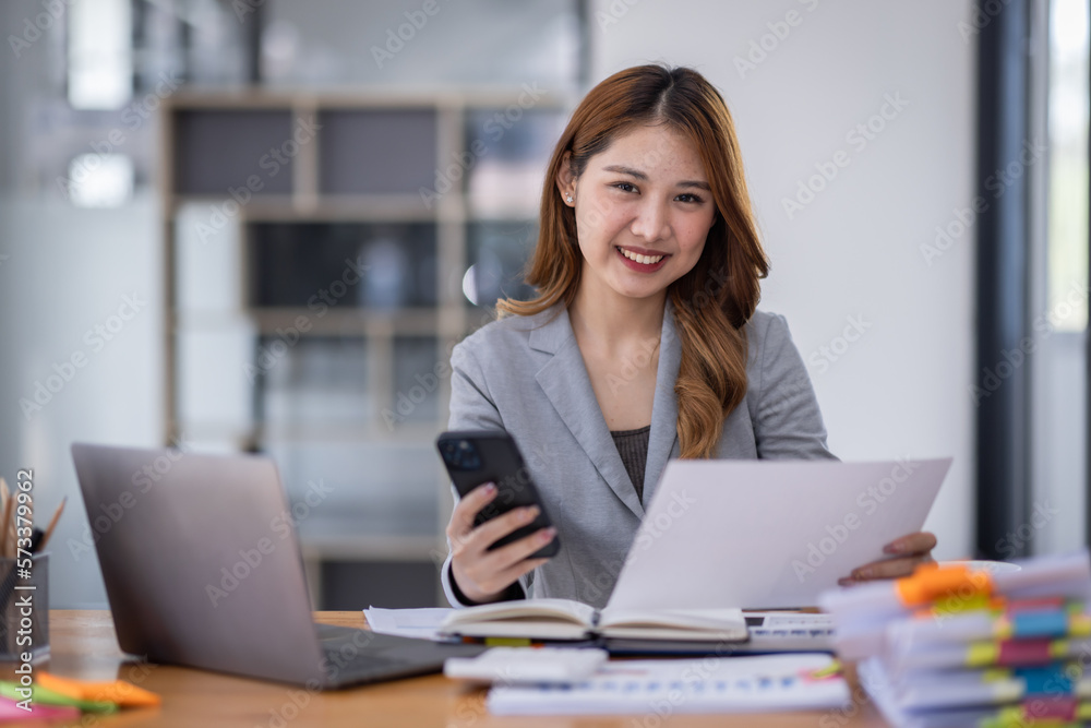 Smiling young Asian business woman executive looking at smartphone using cellphone mobile cell tech, happy ethnic professional female worker working in office typing on cellphone sitting at desk. Smiling young Asian business woman executive looking at smartphone using cellphone mobile cell tech, happy ethnic professional female worker working in office typing on cellphone sitting at desk.