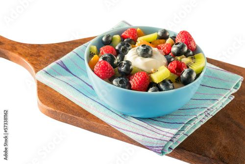 On a kitchen wooden board in a blue bowl  a delicious fresh healthy fruit salad for breakfast.Isolated on a white background.