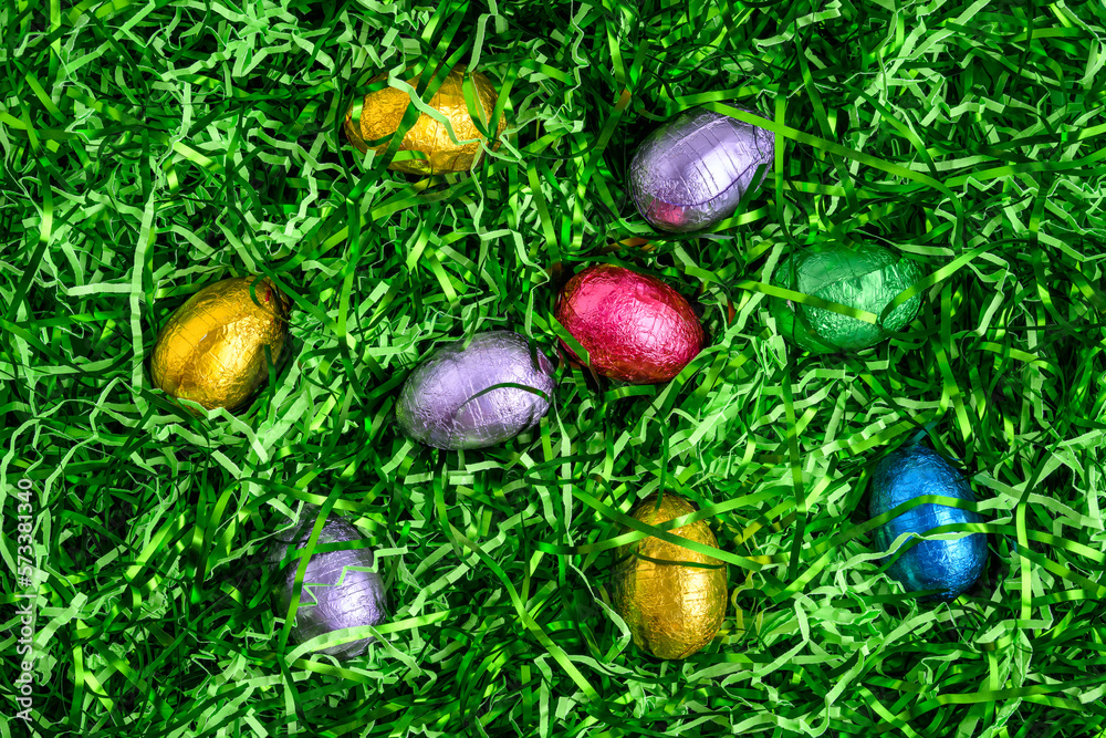 Foil wrapped chocolate easter eggs in a nest of easter grass, as a holiday background
