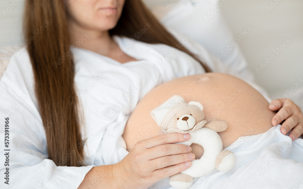 Unrecognizable pregnant woman at home caressing,stroking belly, baby bump, holding cute teddy bear.Cropped, close-up shot.Happy beautiful pregnancy concept Unrecognizable pregnant woman at home caressing,stroking belly, baby bump, holding cute teddy bear.Cropped, close-up shot.Happy beautiful pregnancy concept