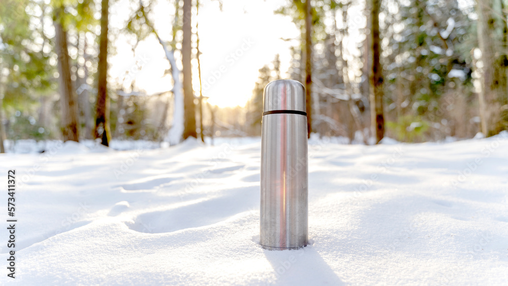 Metal thermos with a hot drink on the background of a winter mountain waterfall. Insulated drink container in the snow Metal thermos with a hot drink on the background of a winter mountain waterfall. Insulated drink container in the snow