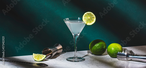 Vodka gimlet alcoholic cocktail drink with vodka, syrup, lime juice and ice, dark green background, bright hard light and shadow pattern, banner photo