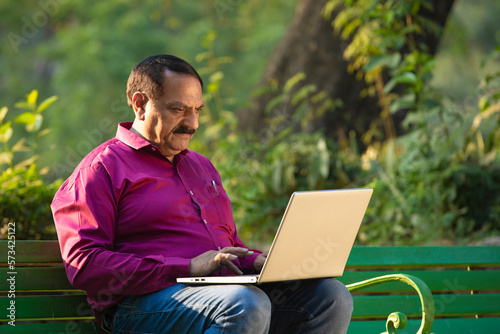 senior indian man using laptop at park.