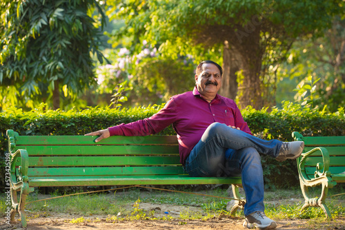 Indian man relaxing on bench in park.