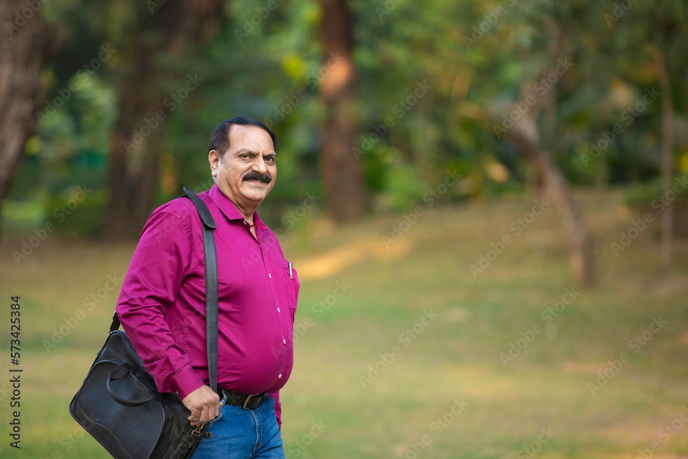 Indian man holding laptop bag and walking at park. Indian man holding laptop bag and walking at park.