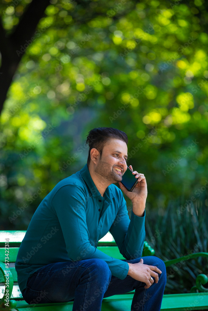 Young indian man talking on smartphone at park. Young indian man talking on smartphone at park.