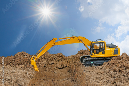 Crawler excavator is digging soil in the construction site with sky and sunlight backgrounds.