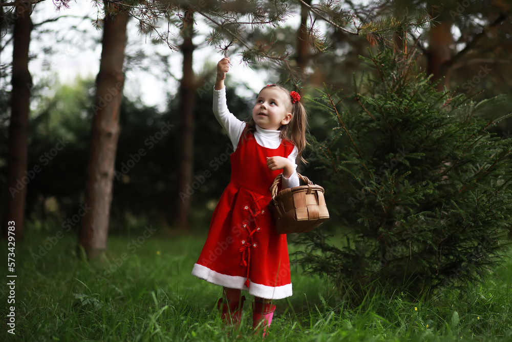A little girl in a red hat and dresses is walking in the park. Cosplay for the fairytale hero 