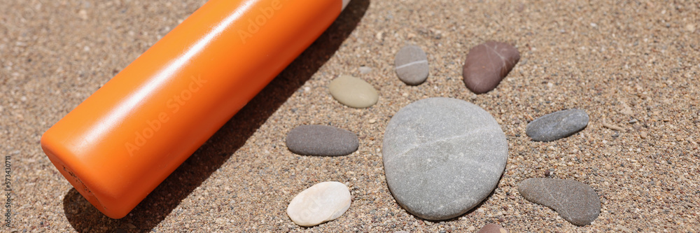 Sun made of stones on sea sand orange liquid bottle of cream or lotion Sun made of stones on sea sand orange liquid bottle of cream or lotion