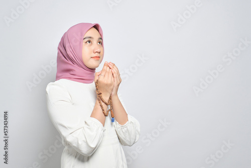 Young Asian Muslim woman praying to god with tasbih isolated over white background