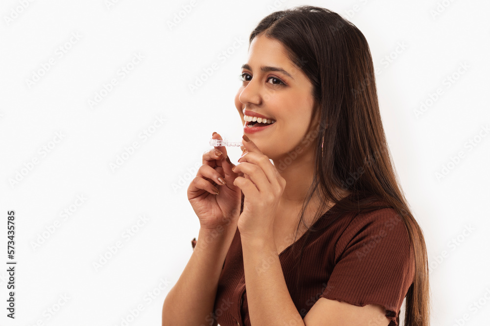 Smiling woman holding teeth aligner against white background Smiling woman holding teeth aligner against white background