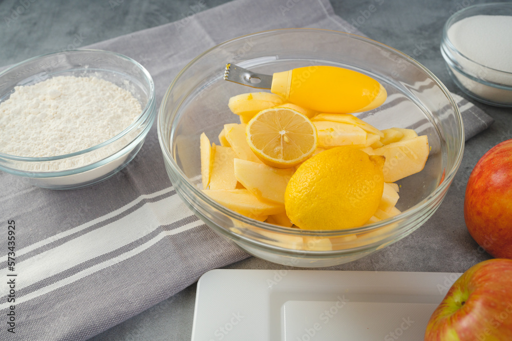 Baking pan with apple slices, lemon, eggs, sugar, and flour in bowls close-up on a kitchen table. Apple cake recipe Baking pan with apple slices, lemon, eggs, sugar, and flour in bowls close-up on a kitchen table. Apple cake recipe