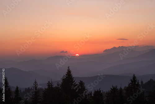 Fading sun hiding behind mountains, spruces silhouettes landscape photo. Beautiful nature scenery photography. Ambient light. High quality picture for wallpaper, travel blog, magazine, article