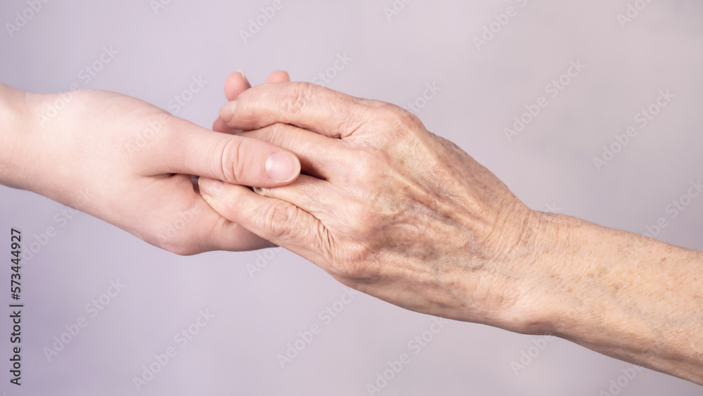 The hand of a young girl reaches for an old hand. Help for the elderly.