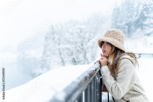 Asian woman tourist in winter coat walking down small town street covered in snow in snowing day. Attractive girl traveler travel local village near the mountain in Japan on winter holiday vacation.