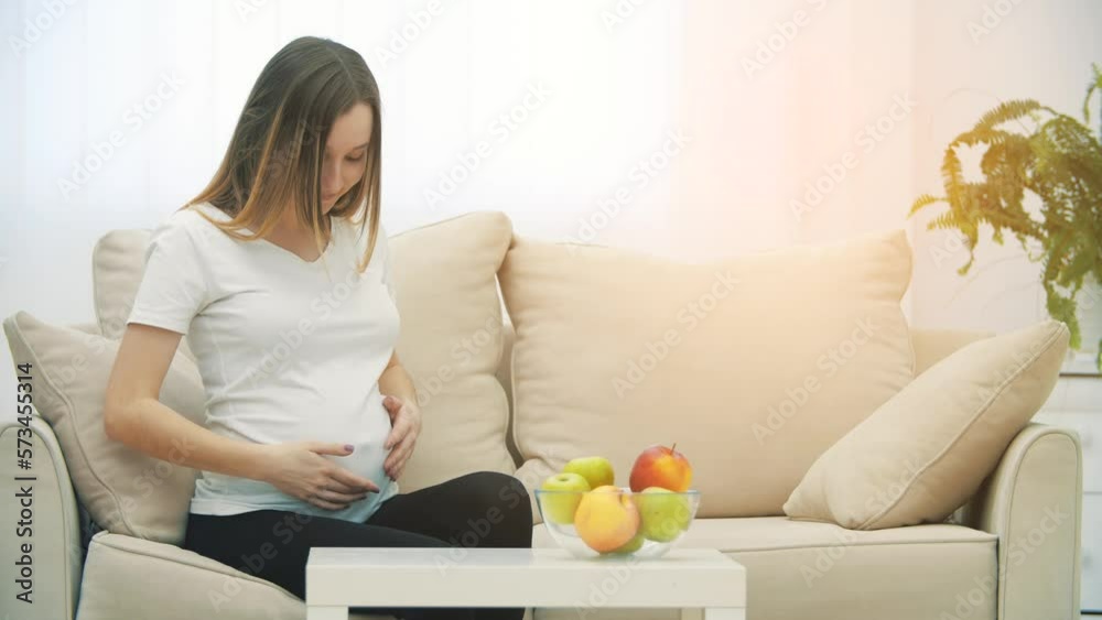 4k slowmotion video of a pregnant woman sitting on white sofa and smiling. 4k slowmotion video of a pregnant woman sitting on white sofa and smiling.
