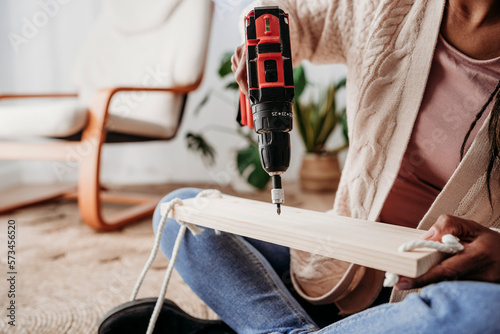 Woman drilling on wood and making diy shelf at home photo