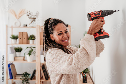 Smiling woman using drill machine on wall at home photo