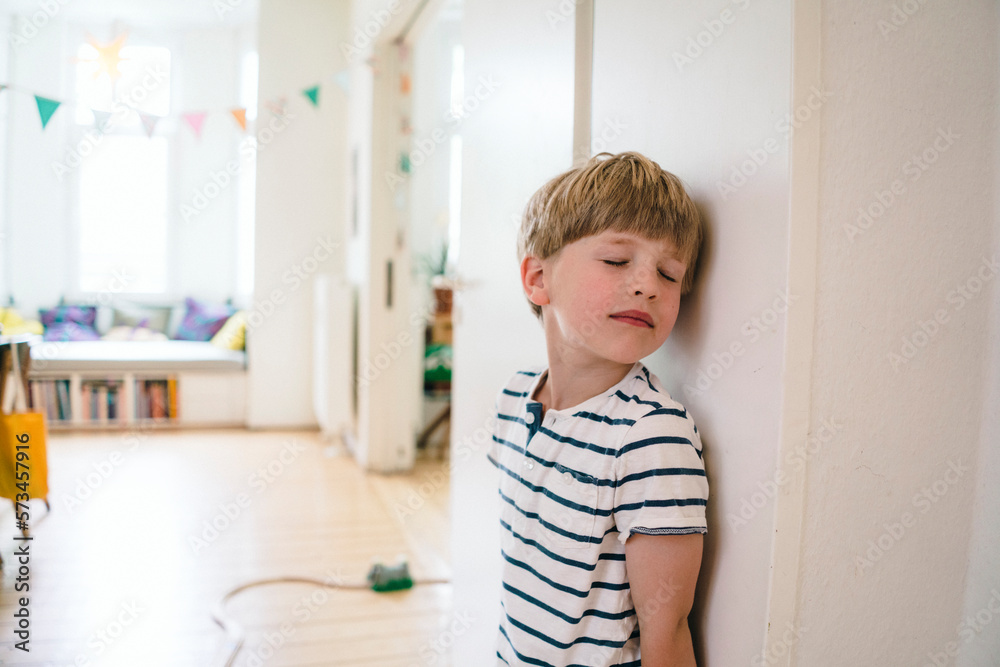 Boy with eyes closed leaning on wall
