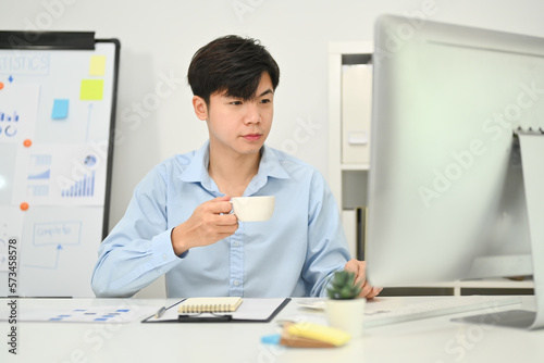 Image of asian businessman drinking coffee and working on marketing project at modern office