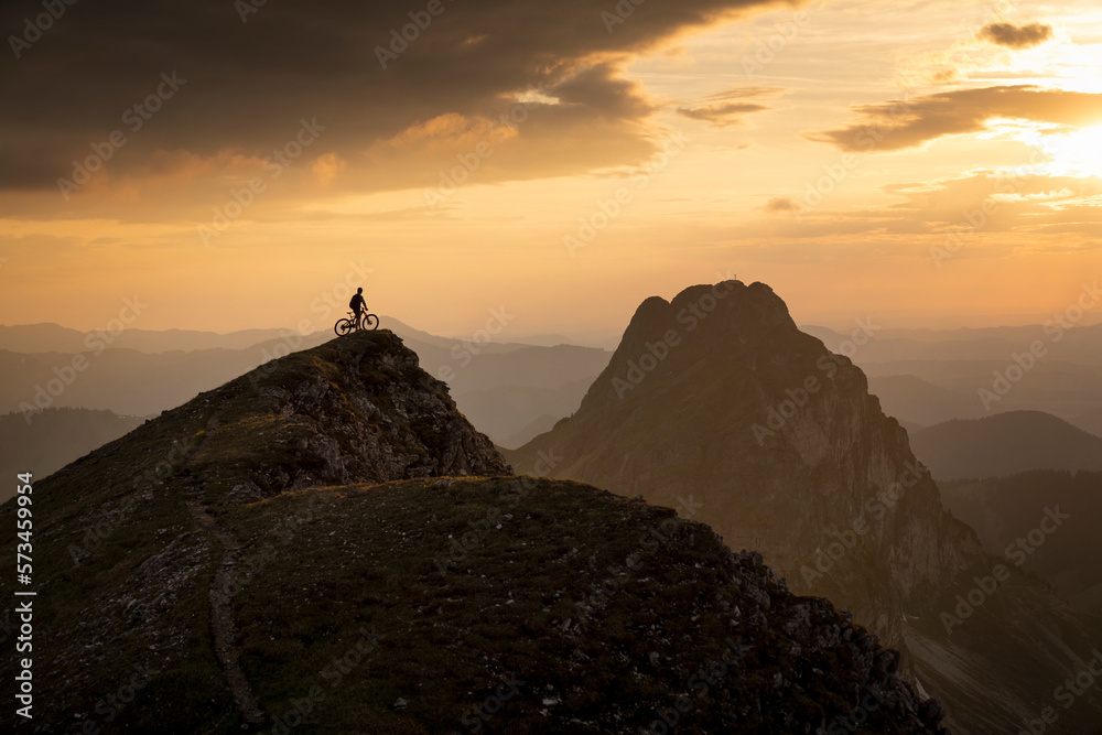 Mountain biker with cycle on top of summit at sunset Mountain biker with cycle on top of summit at sunset