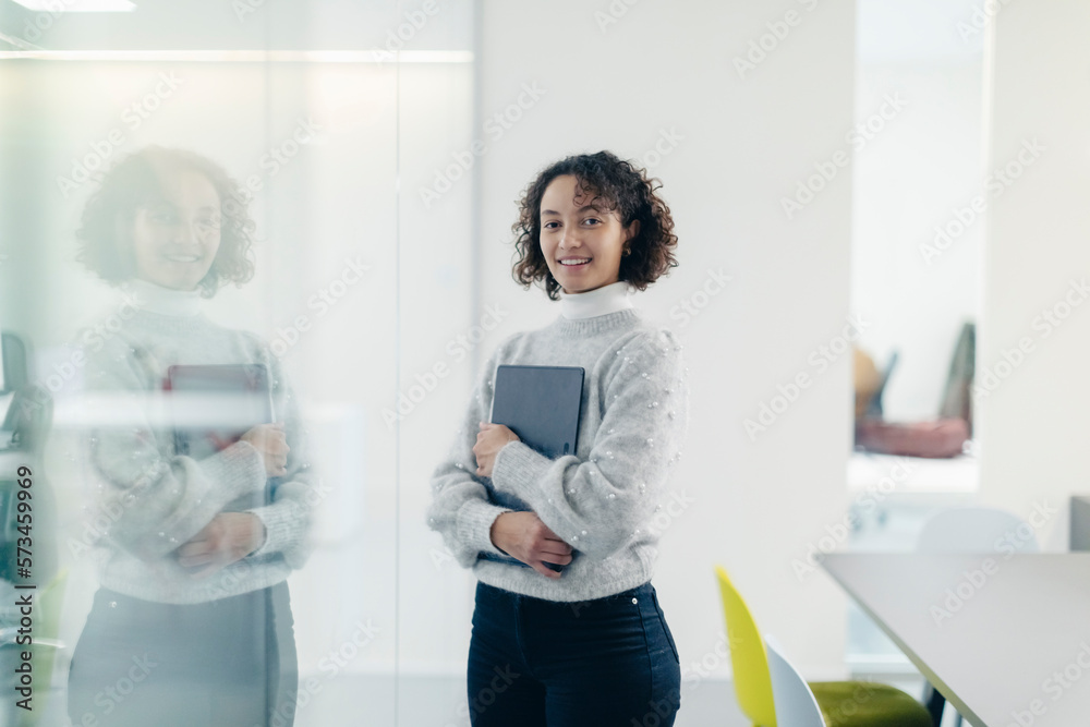 © Westend61 - Smiling young businesswoman with laptop by glass wall at workplace