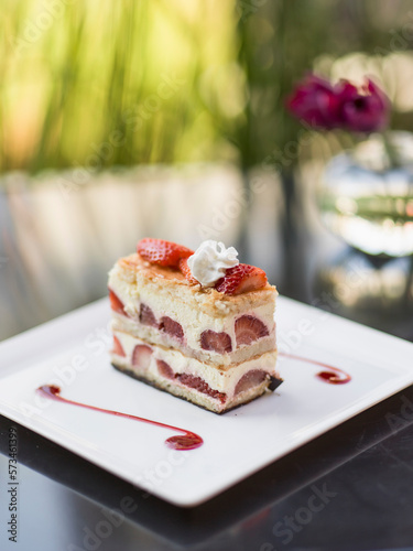 A piece of pastry with strawberry and cream toppings in a serving tray keeps on a tea table.