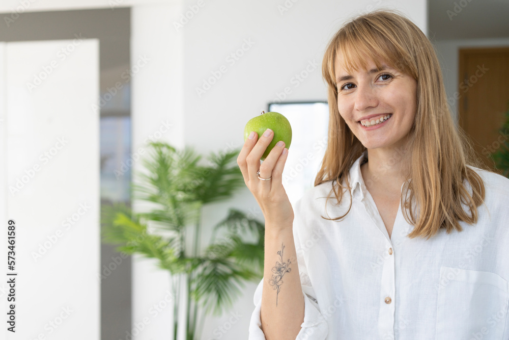 Happy woman with green apple standing at home