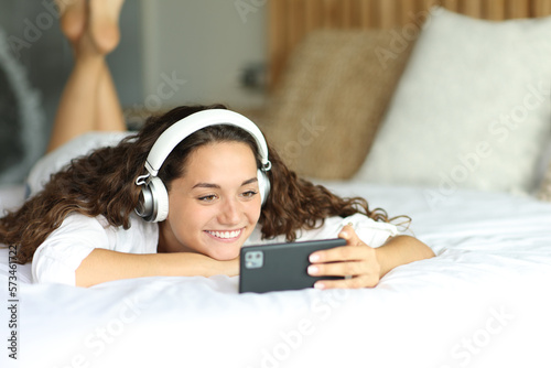 Happy woman watching videos on smart phone on a bed photo