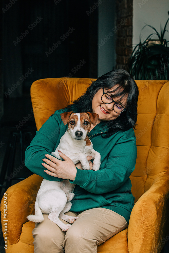 Happy mature woman sitting with dog on armchair Happy mature woman sitting with dog on armchair