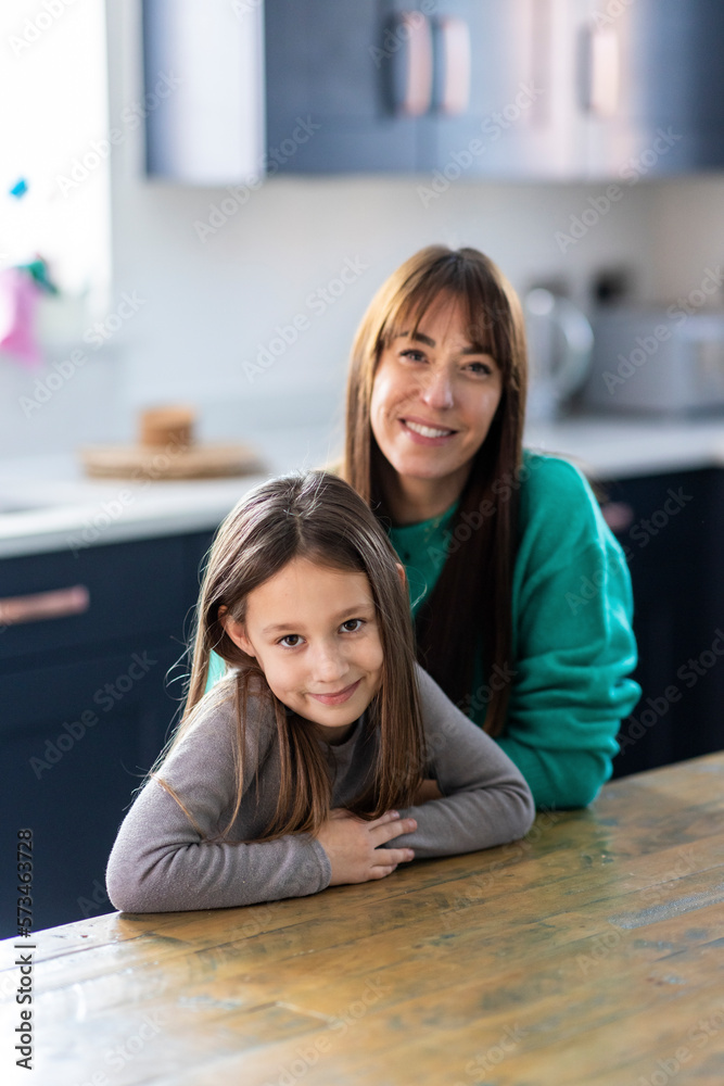 Happy mother and daughter sitting at table in home Happy mother and daughter sitting at table in home