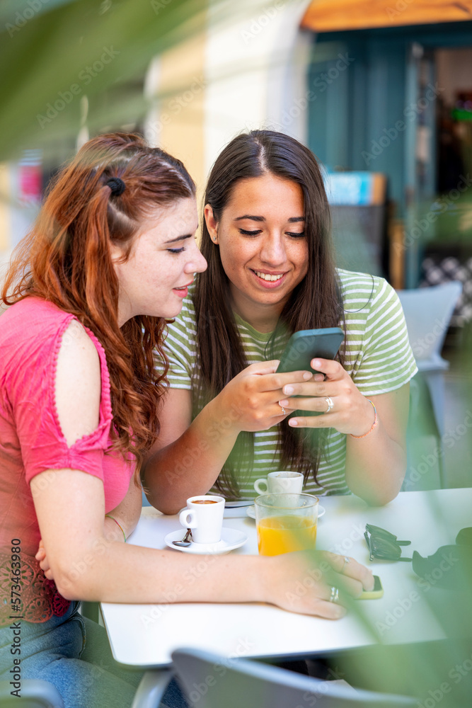 Woman sharing smart phone with girlfriend in sidewalk cafe Woman sharing smart phone with girlfriend in sidewalk cafe