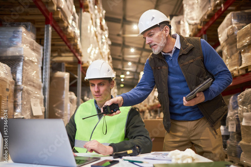 Portrait of two male workers using laptop in warehouse while managing distribution