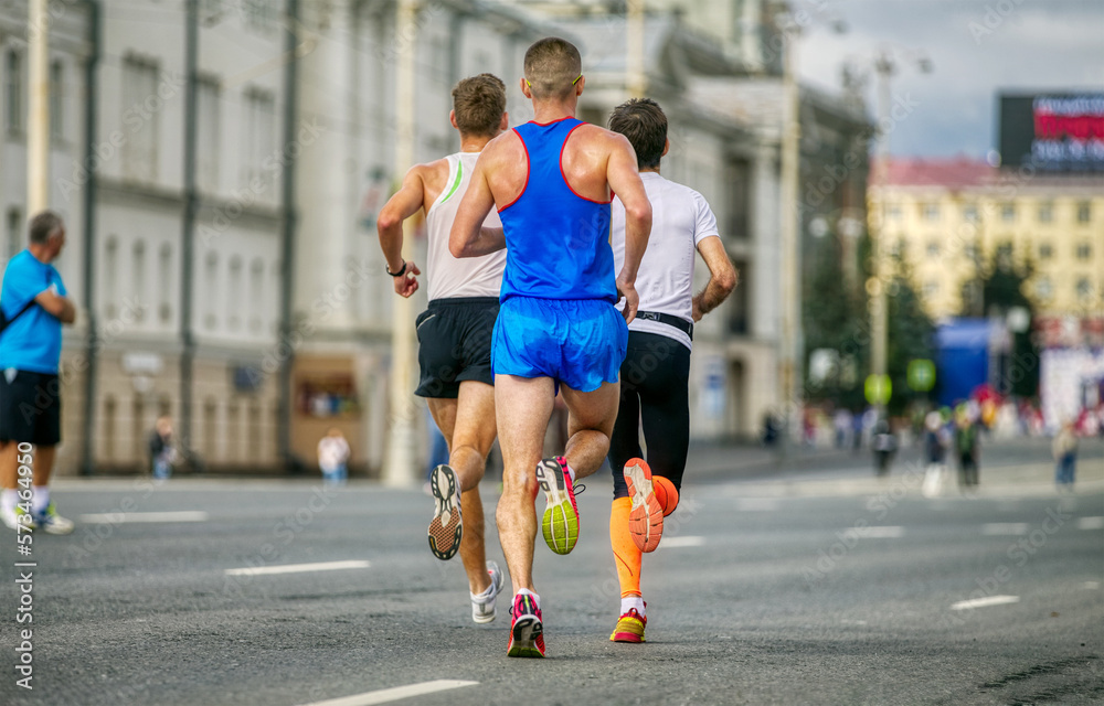 back three male athletes runners run marathon on avenue