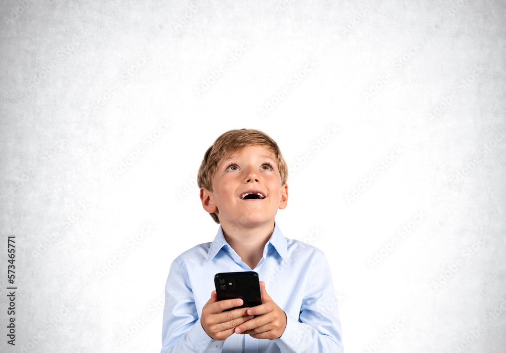 Happy boy with phone in hands look up, copy space grey backgroun Happy boy with phone in hands look up, copy space grey backgroun