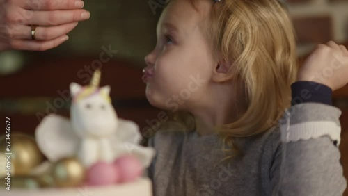Birthday girl distracted with mothers attention while eating sweets, autistic kid, pink fancy cake with unicorn and chocolate balls.Pretty blond child,watching and chewing.party time,celebrating.HQ 4k