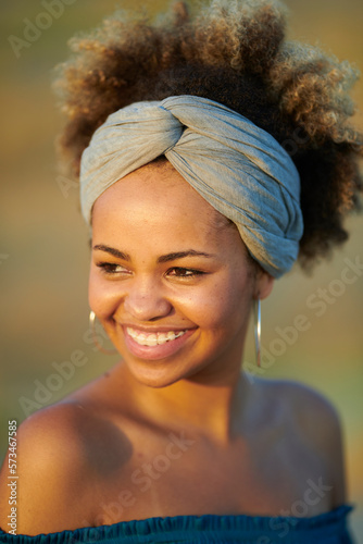 Stylish woman with brackets in band. Headshot of beautiful smiling woman with dyed hair in band and big hoops with bare shoulders smiling warmly away in sunlight.
