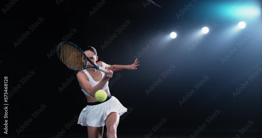 Aesthetic Shot of an Athletic Female Tennis Player with a Black Background Hitting a Low Ball Under Spotlights. Cinematic Super Slow Motion Captures a Winning Strong Forehand Shot in a Championship