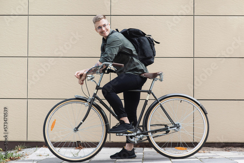 Young handsome man with bike over beige wall background in a city, Smiling student man with bicycle smiling outdoor, Modern healthy lifestyle, travel, casual business concept